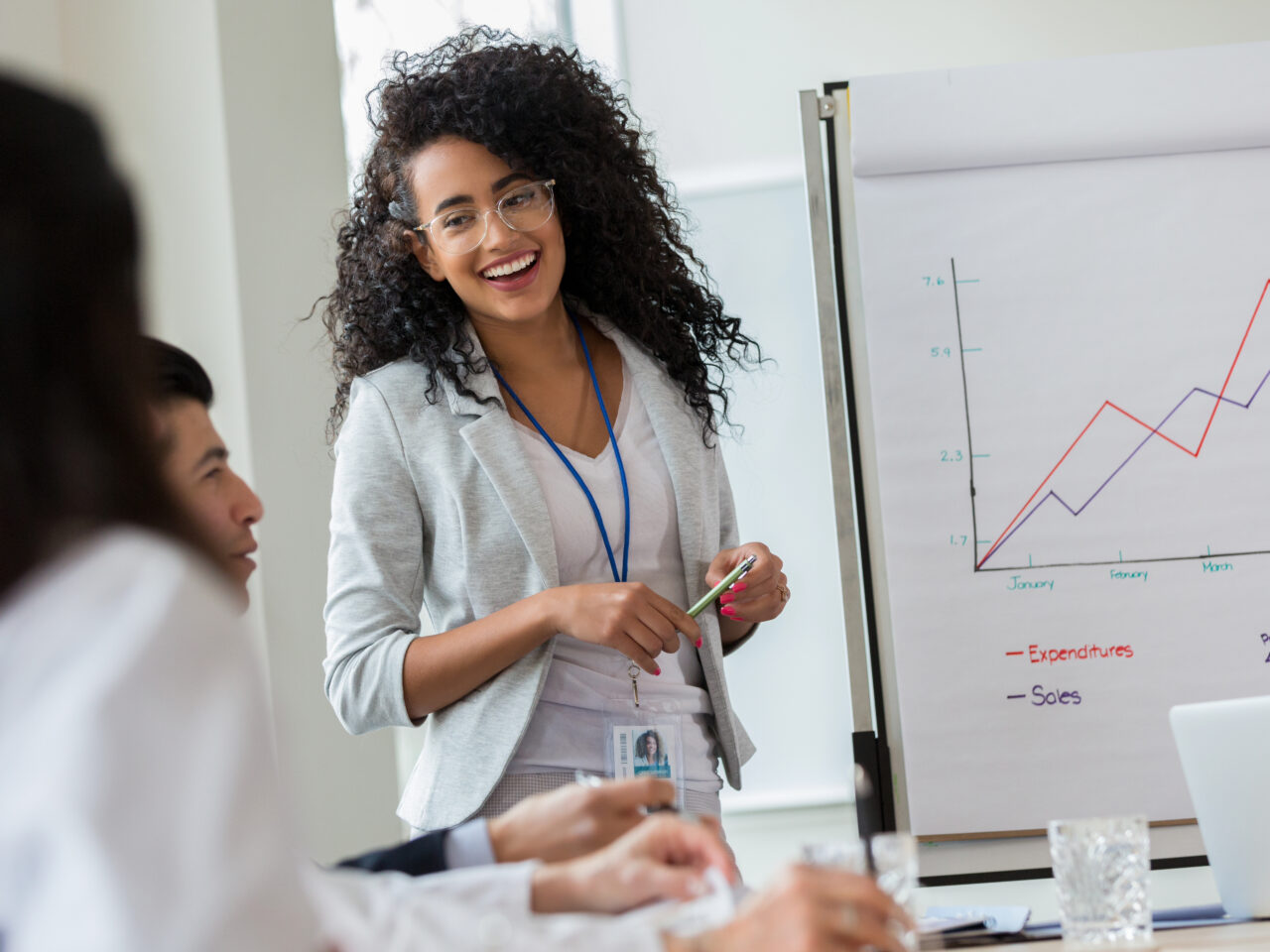 Confident young businesswoman gives presentation to colleagues. She is standing in front of a growth chart.